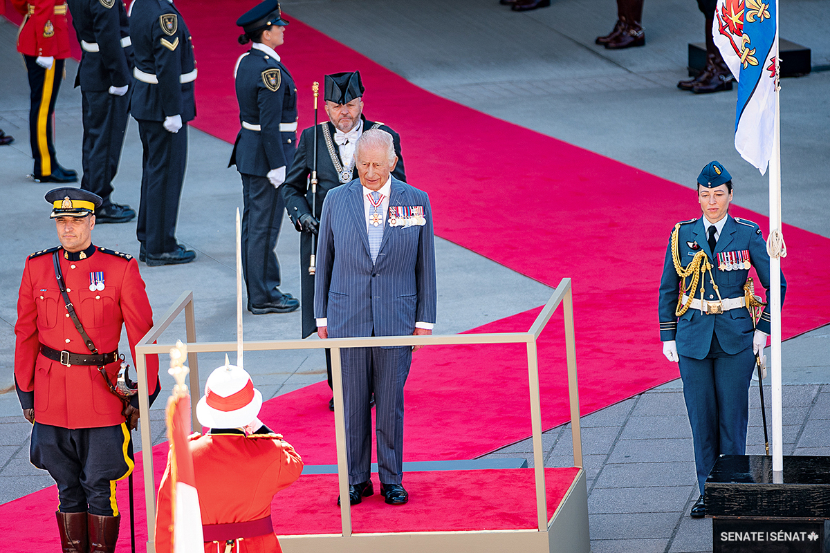 The King prepares to inspect his guard of honour outside the Senate of Canada Building. The personal Canadian flag of the monarch is just visible hanging from the flagpole.