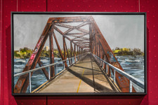 Une peinture encadrée représentant un vieux pont ferroviaire recouvert de graffitis.