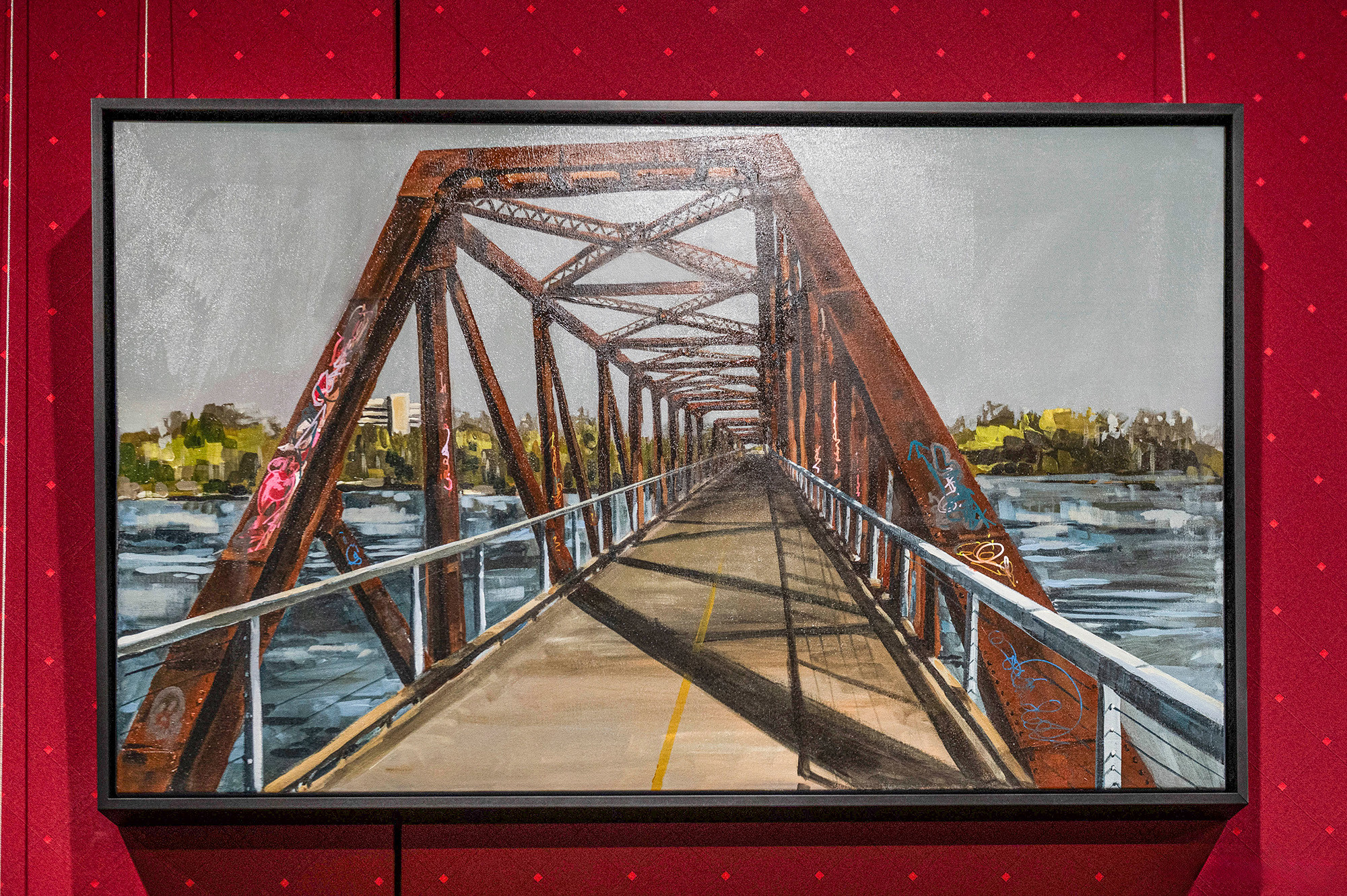 A framed painting of an old railway bridge painted with graffiti. 