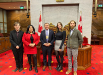 Senator Brian Francis and four students stand in front of the Speaker’s dais in the Senate Chamber.