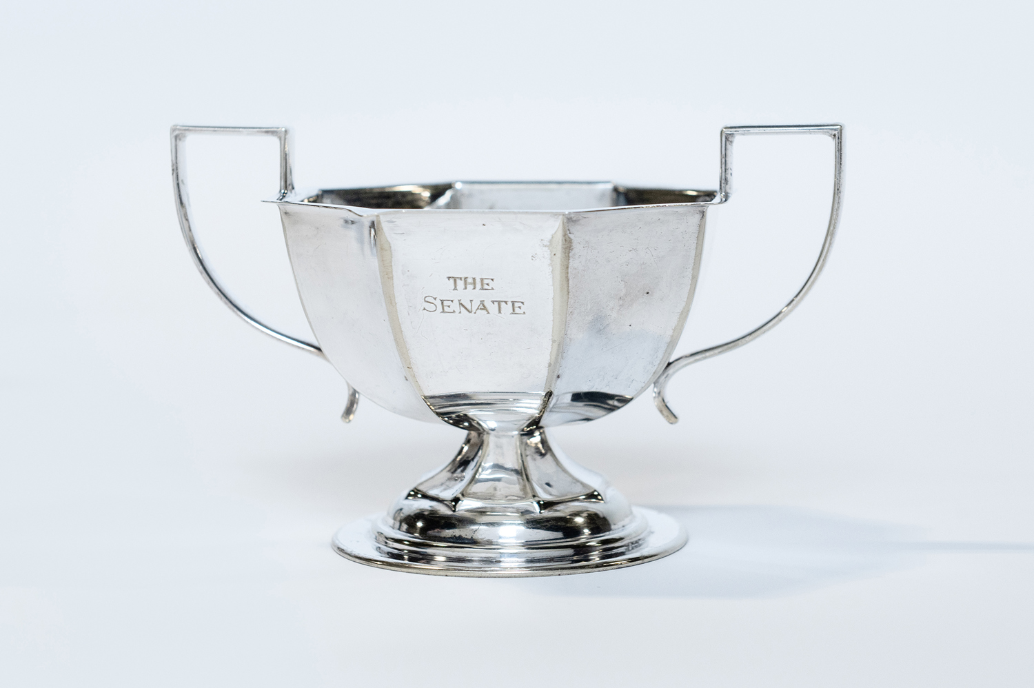 A silver sugar bowl with two handles, engraved with “The Senate” on the side.