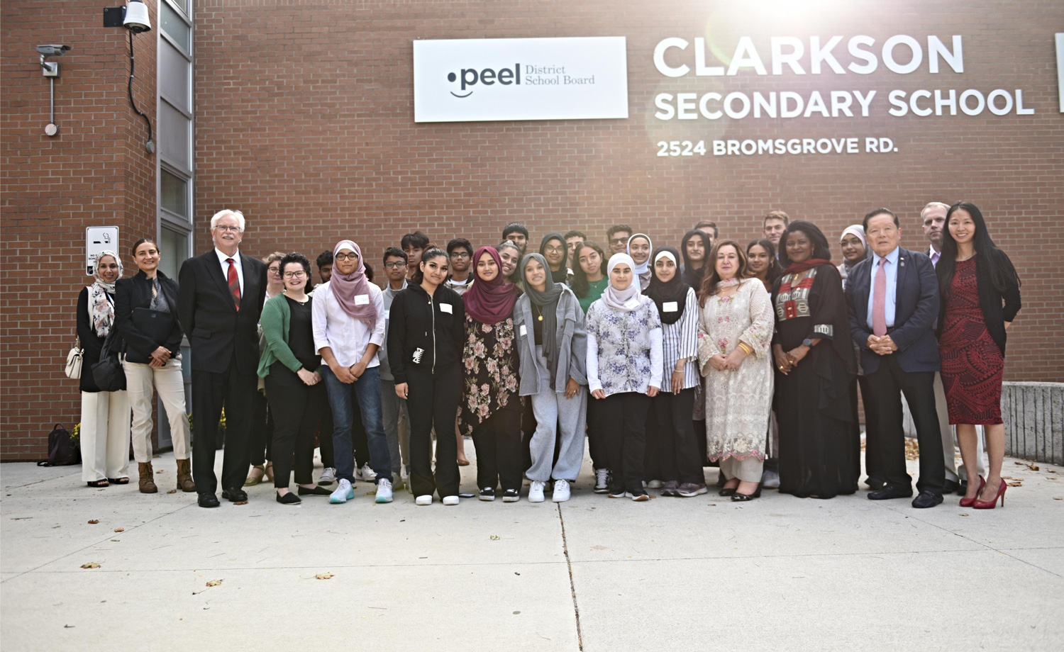 A group of adults and students pose in front of Clarkson Secondary School.