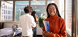 A young Black woman wearing glasses and an orange turtleneck holding a folder in an office.