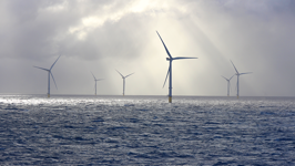 Beams of sunlight illuminate six wind turbines in an offshore wind farm.