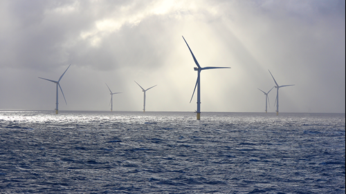 Beams of sunlight illuminate six wind turbines in an offshore wind farm.