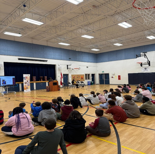 A group of students sitting on the floor in a gym.