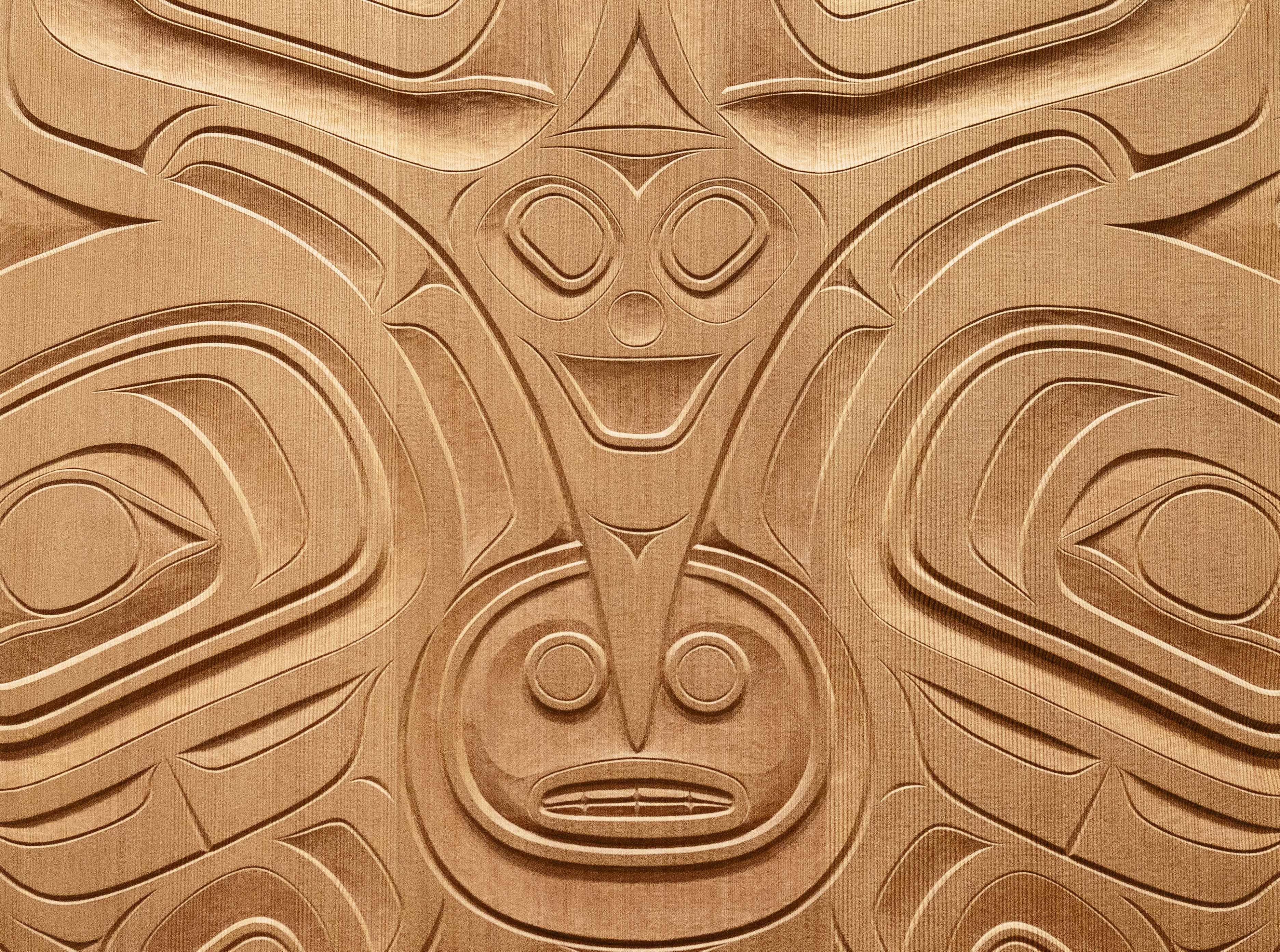 A wooden carving featuring figures from Haida mythology, including a raven holding a figure in its beak.