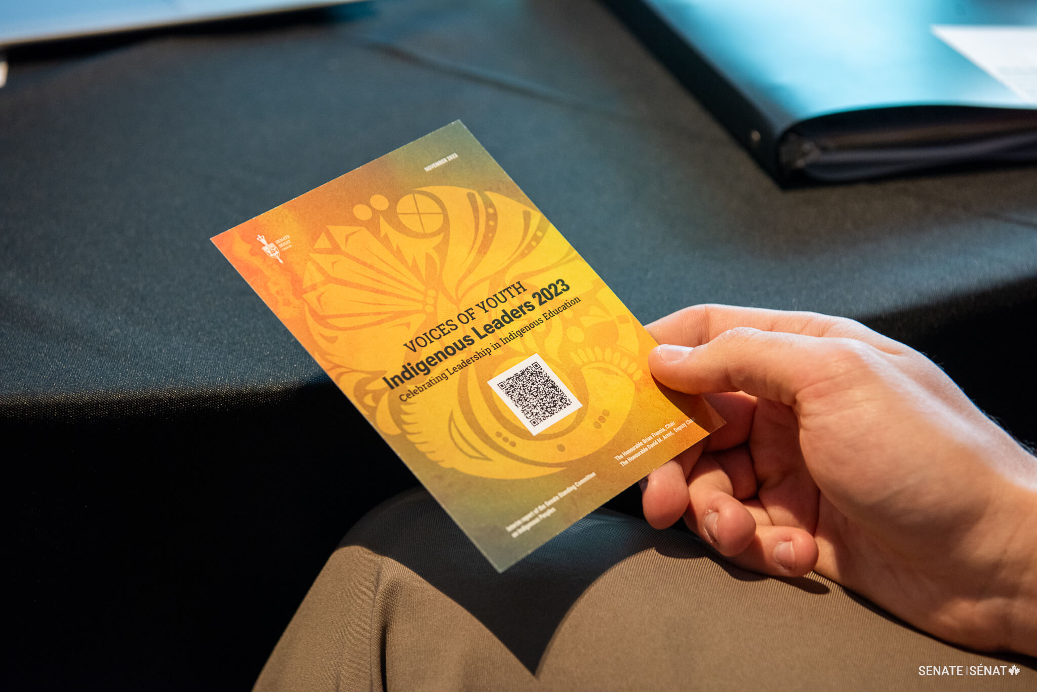 Une personne tient une carte postale montrant la couverture du rapport lors d’une session du Rassemblement national pour l’éducation autochtone.