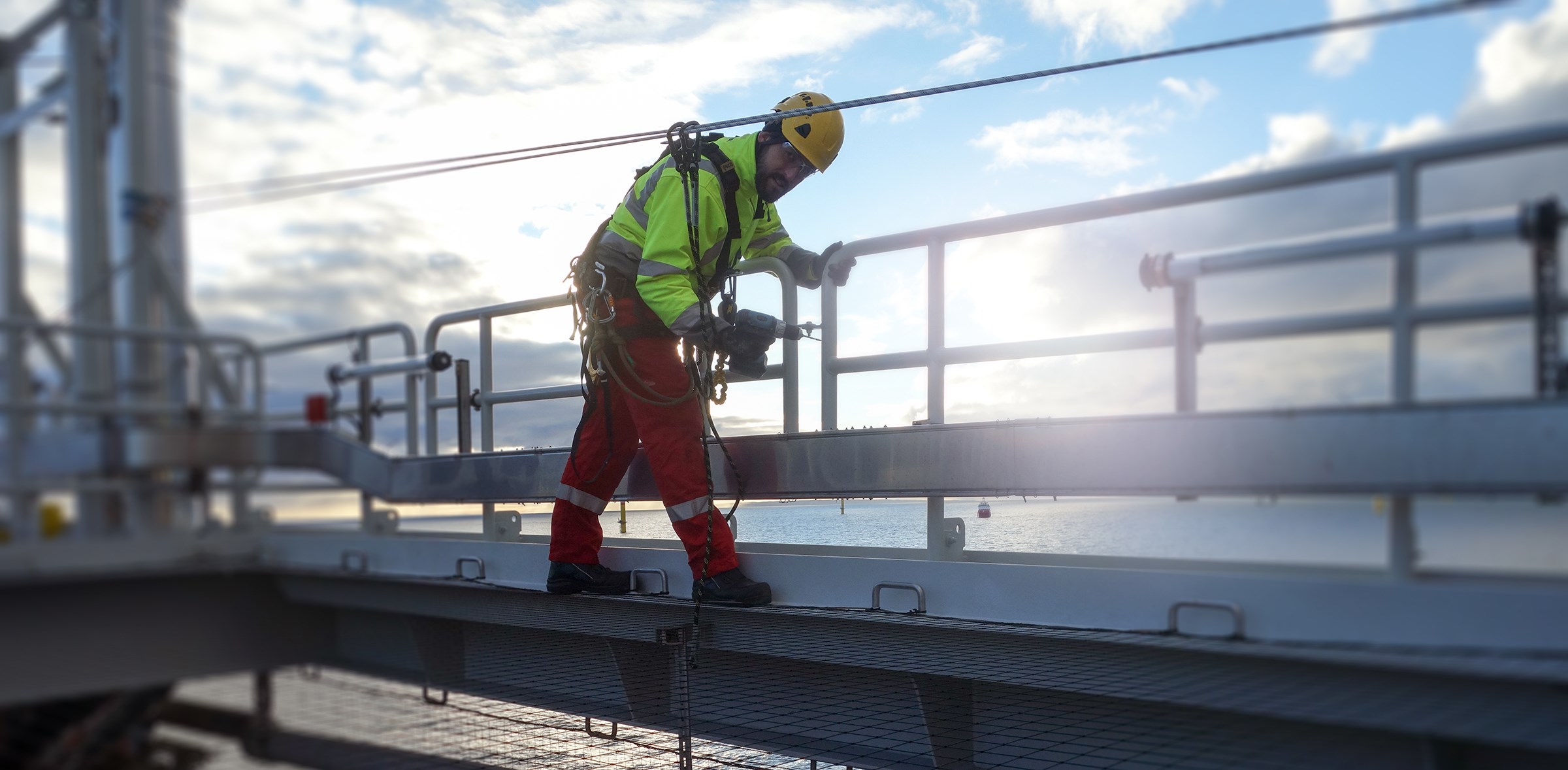 A worker wearing a helmet, neon jacket and orange pants walks across a platform on an offshore oil rig.