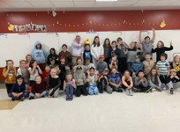 Le sénateur David M. Wells tient un canard en caoutchouc jaune sur la tête d’un garçon, et un groupe d’enfants font des grimaces en posant dans une salle de classe.