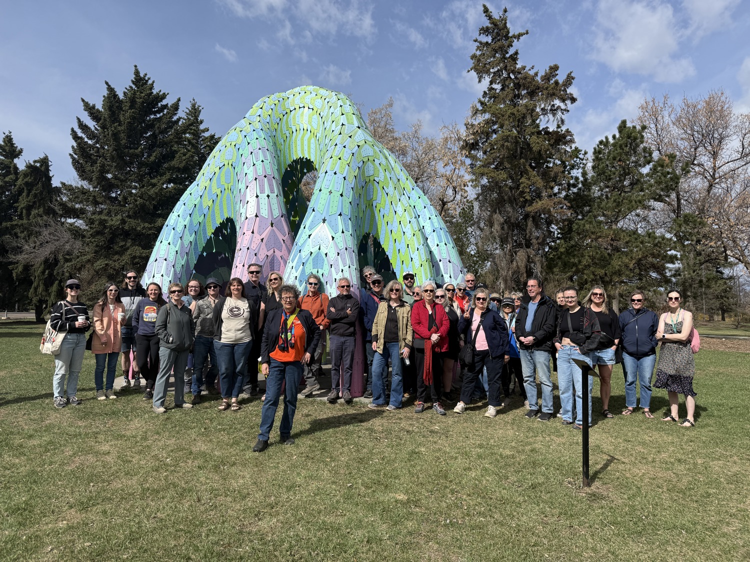 Un grand groupe de personnes pose pour une photo devant une sculpture colorée dans un parc.