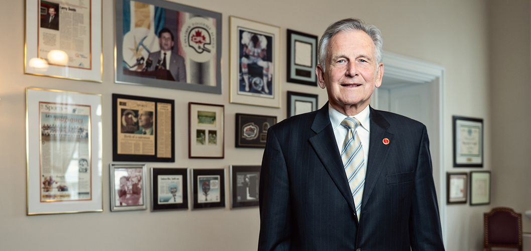 A man stands in an office before a wall of photos and newspaper clippings.