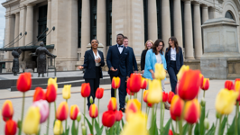 Six students dressed in business attire walking and smiling outside the Senate of Canada Building, with tulips in the foreground.