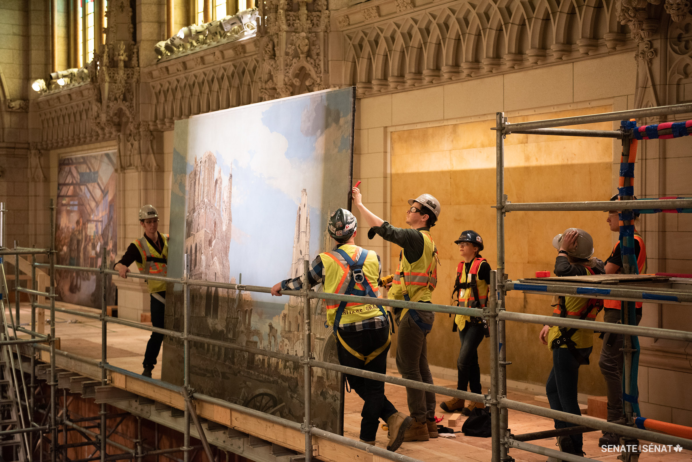 Conservators take down James Kerr-Lawson’s The Cloth Hall, Ypres (1919) from the walls of the Senate Chamber in Centre Block. (CWM 19710261-0334, Beaverbrook Collection of War Art, Canadian War Museum)