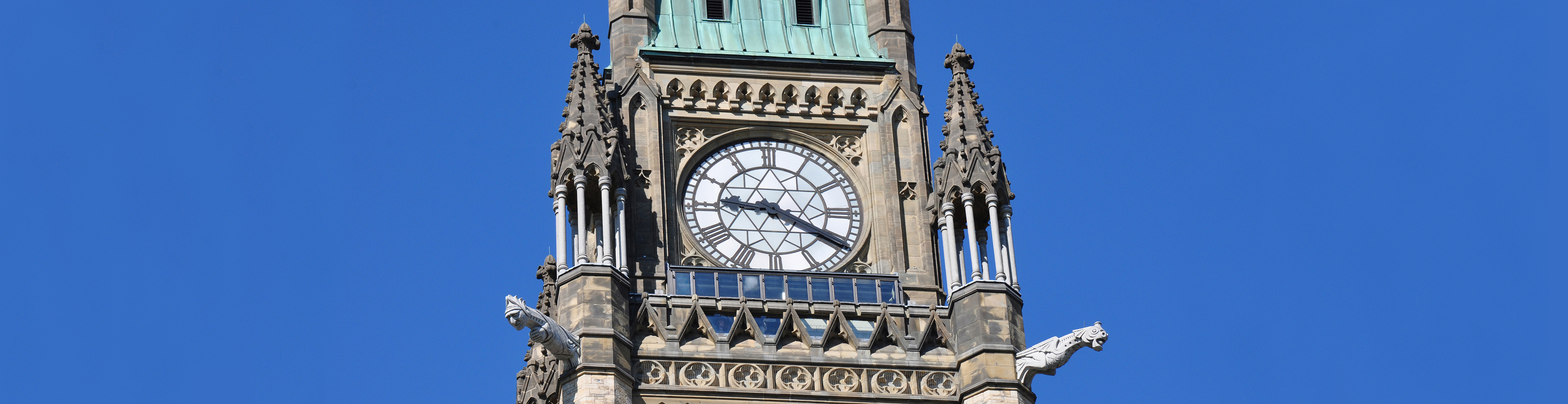The top of Canada’s Peace Tower, with gargoyles, a large clock face, conical turrets and a green copper roof.