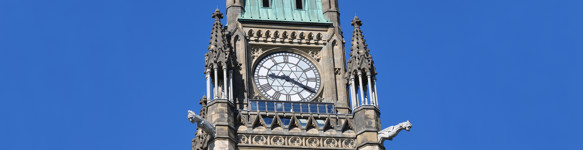 The top of Canada’s Peace Tower, with gargoyles, a large clock face, conical turrets and a green copper roof.