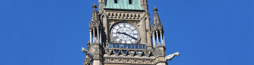 Le sommet de la Tour de la Paix du Canada. On aperçoit des gargouilles, un grand cadran d’horloge, des tourelles coniques et un toit de cuivre vert.