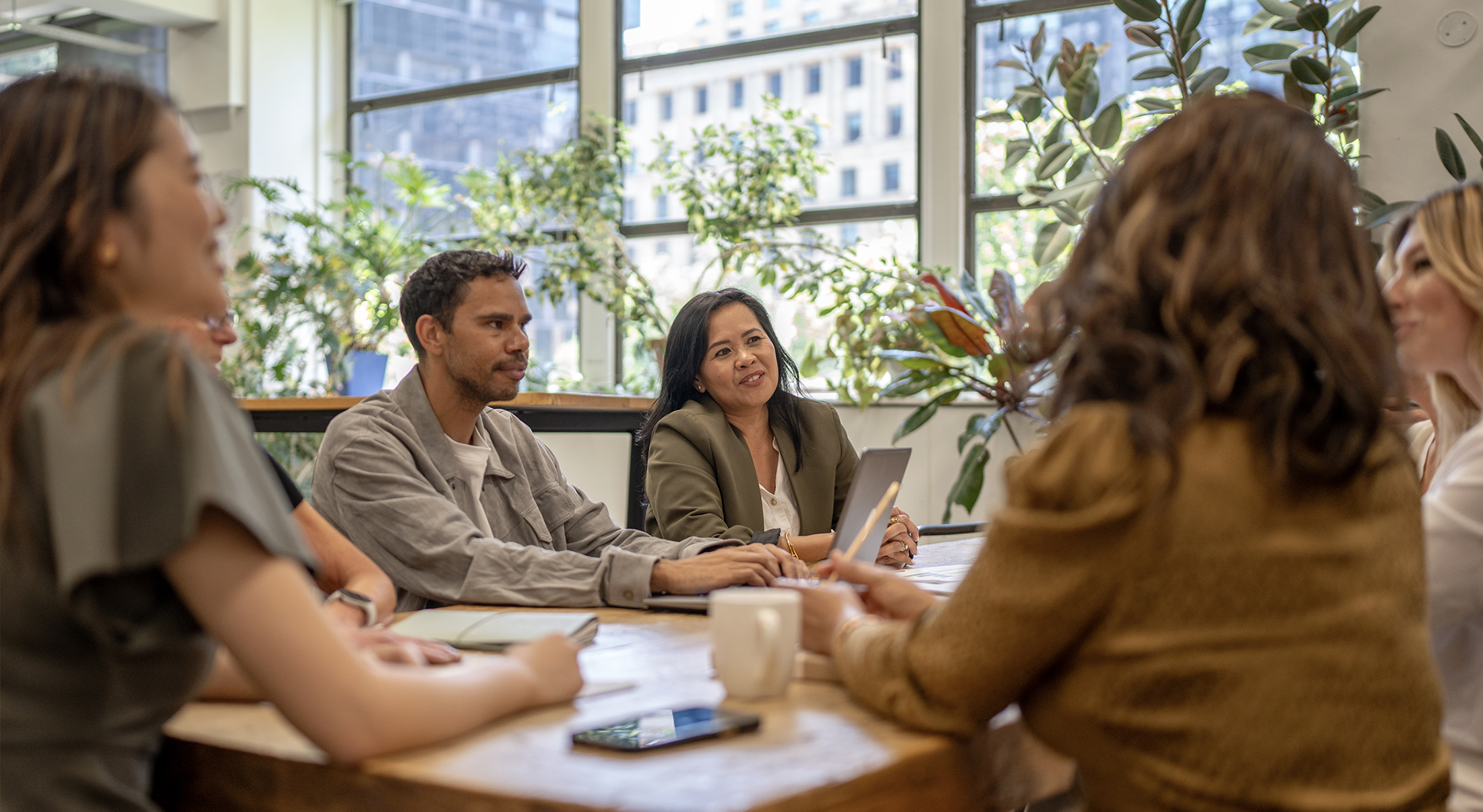 Four women and a man sitting around a table and talking in an office.