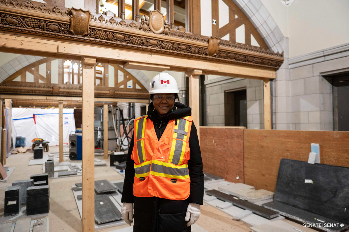 Une femme portant un équipement de protection individuelle se tient debout au centre des travaux de construction de l’édifice du Centre sur la Colline du Parlement.