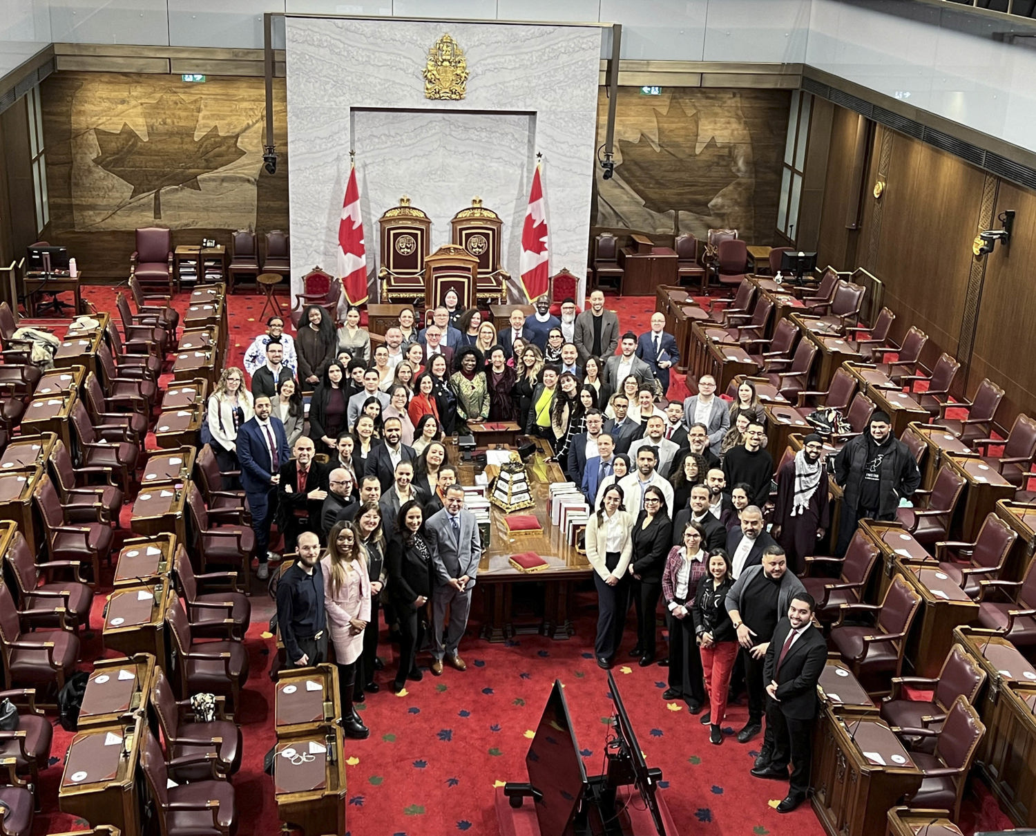 Un grand groupe de personnes se fait prendre en photo autour d’une table dans la Chambre du Sénat.