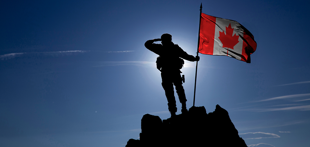 Silhouette en contre-jour d’un soldat debout au sommet d’une montagne et tenant un drapeau canadien hissé sur un mât.