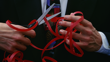 A man’s hands holding scissors that are cutting red tape.