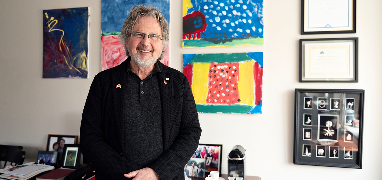 A man stands in an office before a wall of colourful children’s paintings. 