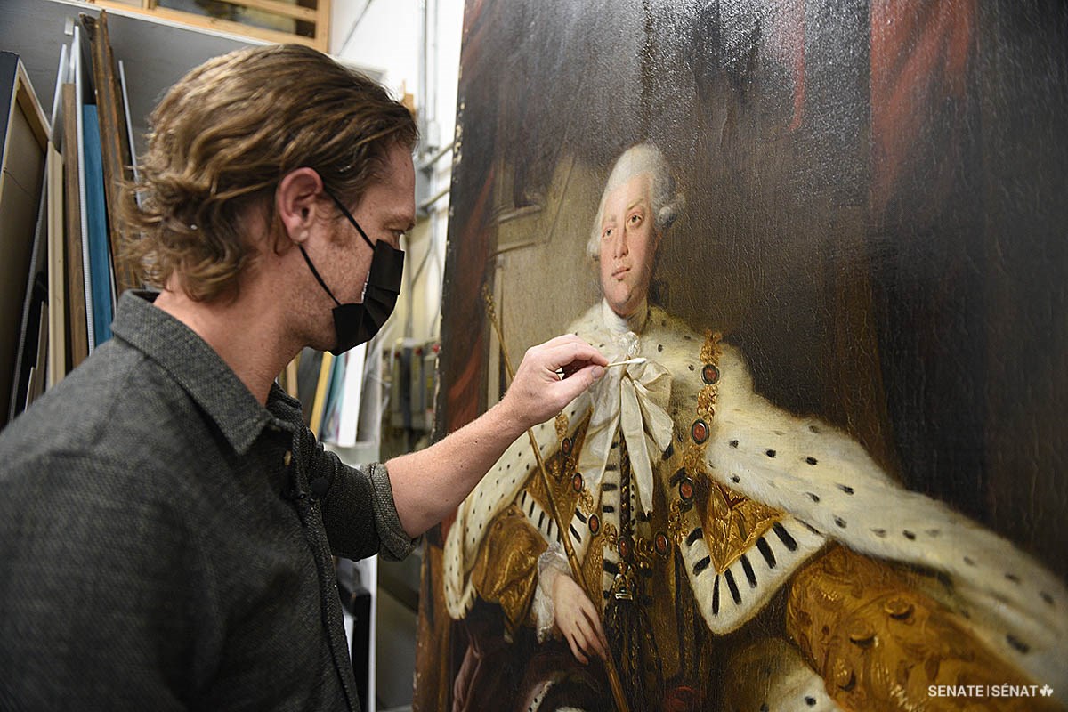 Conservator David Legris uses a cotton swab and mild solvents to gently remove surface grime and layers of yellowed varnish from the Senate’s portrait of King George III.