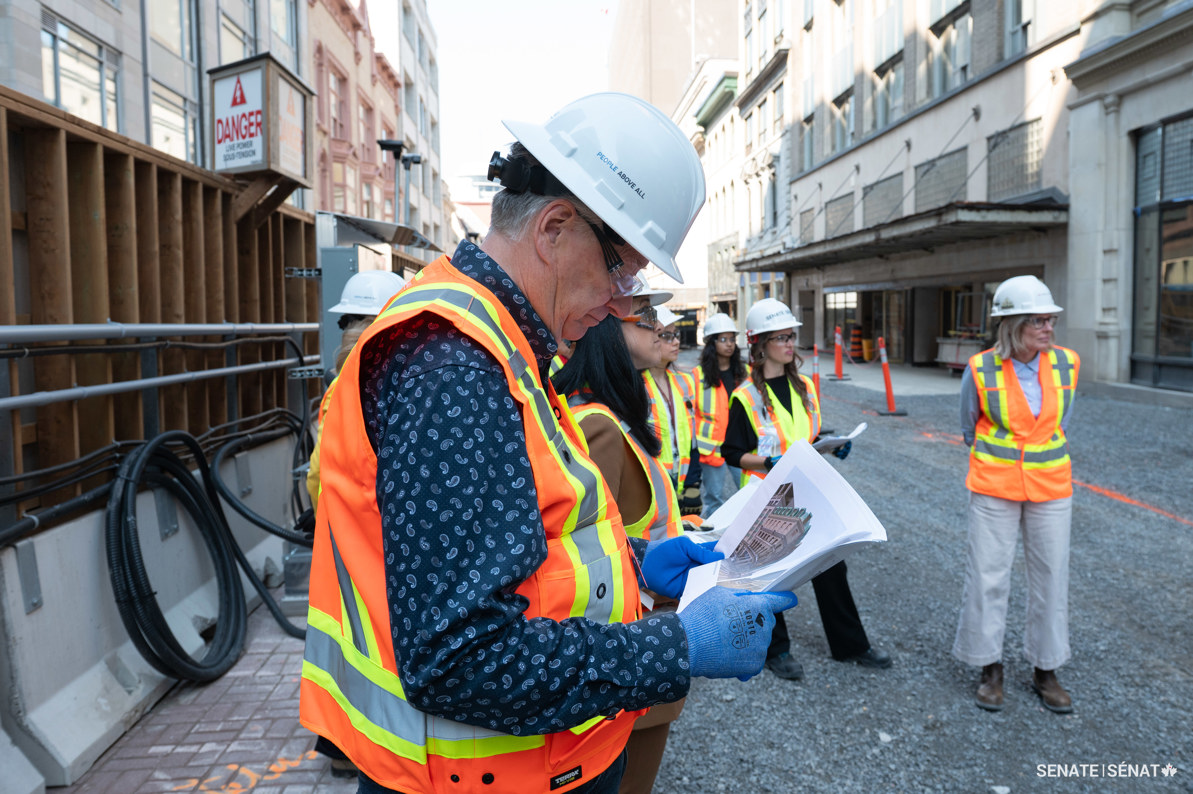 Un homme portant un équipement de protection individuelle lit une pile de documents sur un chantier de construction dans le centre-ville d’Ottawa.