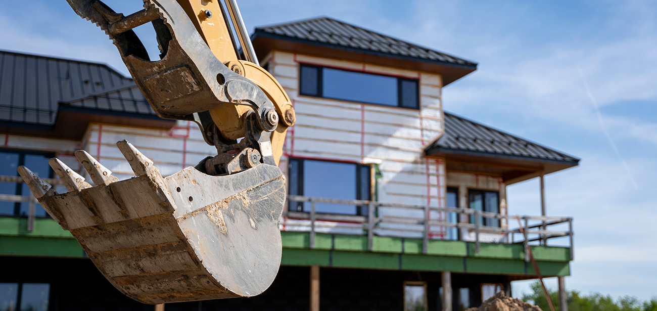 An excavator bucket in front of a home under construction.