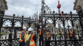 A pair of large, black, partially opened iron gates in front of Centre Block on Parliament Hill, surrounded by people wearing personal protective equipment.