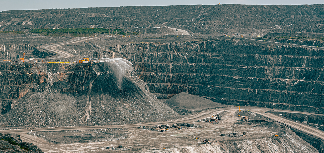 Wide view of an industrial, open-pit gold mine, showing heavy machinery spraying water on crushed rock.