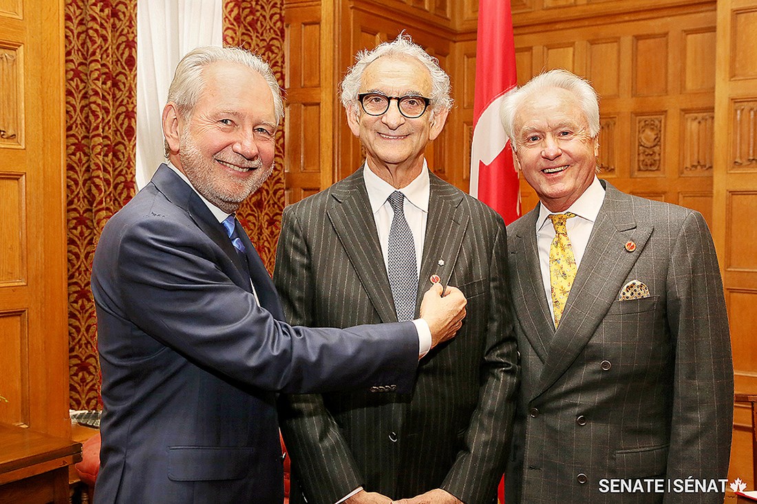 Le sénateur V. Peter Harder (à gauche) montre la nouvelle épinglette du sénateur Howard Wetston lors de sa cérémonie d’assermentation en décembre 2016. On voit également sur la photo l’honorable Doug Black, ancien sénateur.