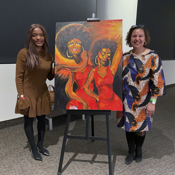 Deux femmes sont debout à côté d’un tableau.