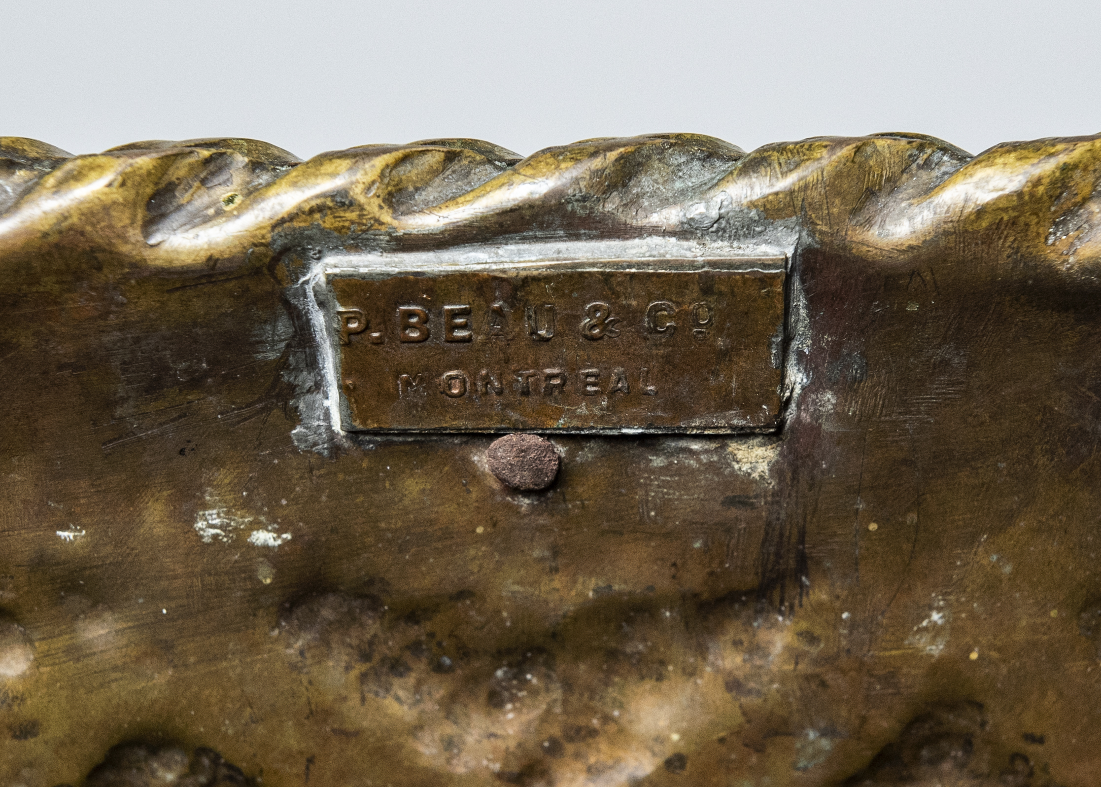 A maker’s tag on the inside of a brass planter that reads “P. Beau & Co. Montreal.”