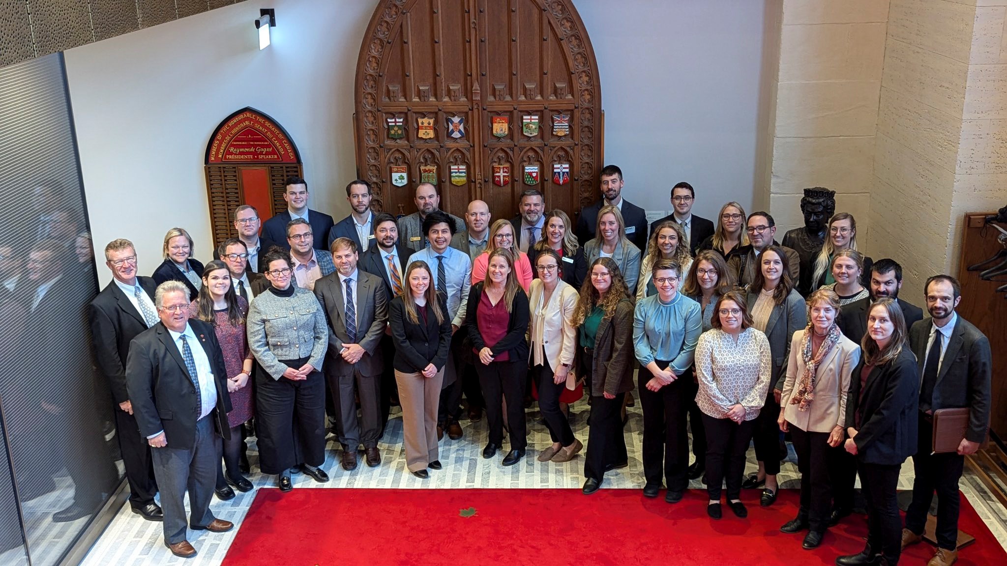 A large group of people pose outside the Senate Chamber in the Senate of Canada Building.