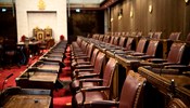 Rangées de bureaux des sénateurs dans la Chambre rouge de l’édifice du Sénat du Canada, avec les trônes du Sénat en arrière-plan.