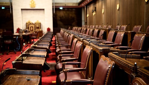 Rows of senators’ desks in the Red Chamber in the Senate of Canada Building, with the Senate thrones in the background.