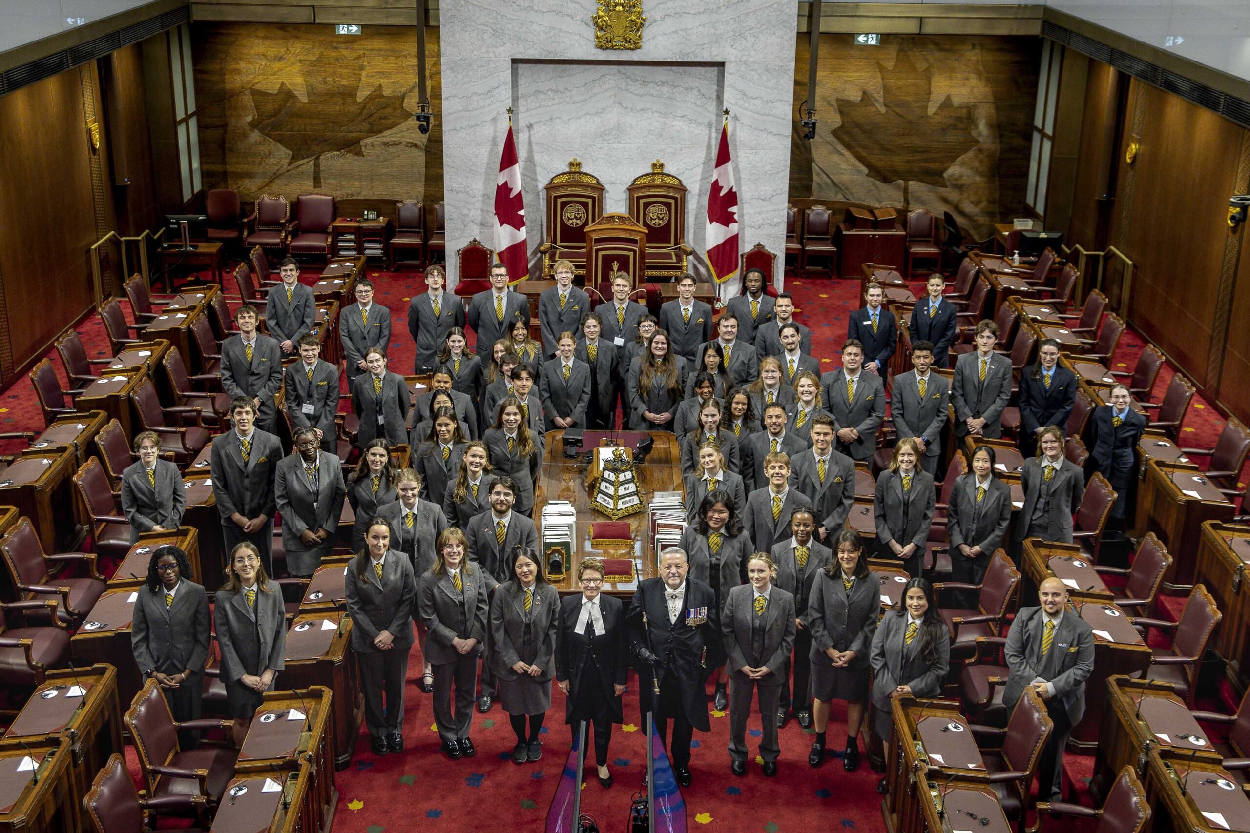 Un grand groupe de personnes se fait prendre en photo autour d’une table dans la Chambre du Sénat.