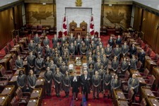Un grand groupe de personnes se fait prendre en photo autour d’une table dans la Chambre du Sénat.