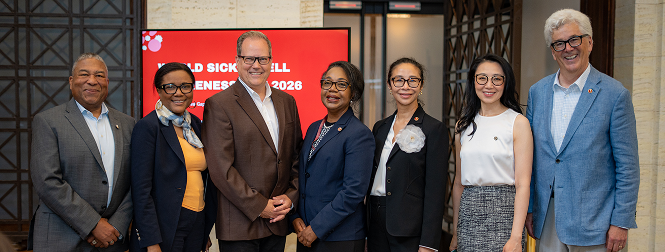 Men and women stand in front of a digital sign for an event about sickle cell disease.