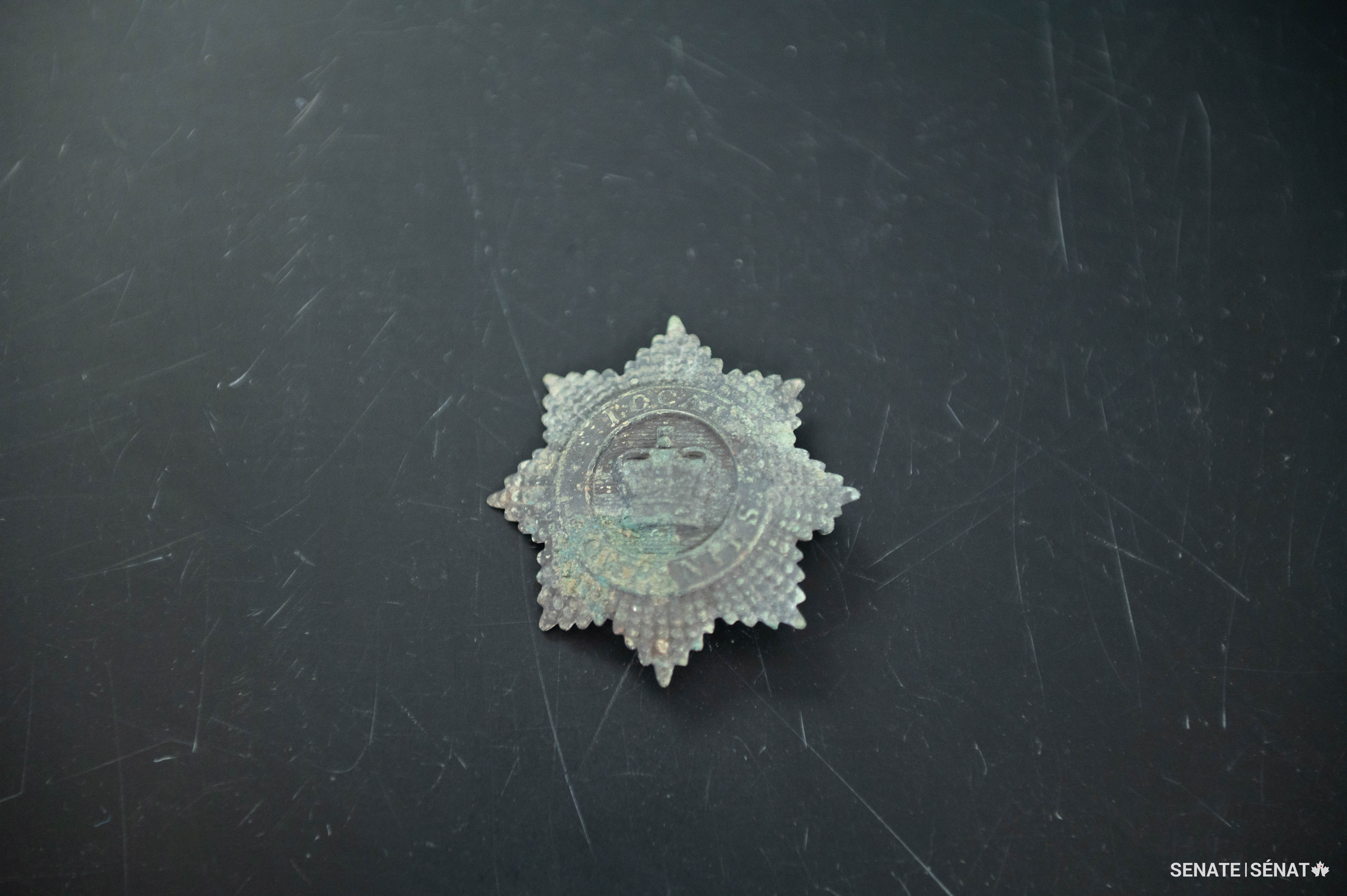 Cet insigne décoratif appartenait à des membres de la Enrolled Pensioner Force, une compagnie militaire qui était stationnée sur Barrack Hill de 1854 à 1858. Il se fixait à l’avant d’un chapeau cylindrique appelé « shako » que les militaires portaient comme partie de leur uniforme.