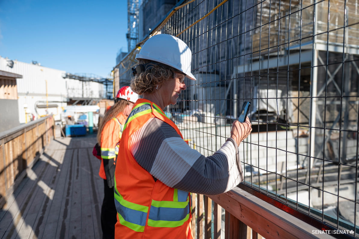 Une femme portant un équipement de protection individuelle prend une photo avec son téléphone intelligent sur le chantier de la Colline du Parlement.