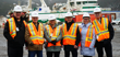 Four men and two women in high-visibility vests and hard hats standing near a ship.