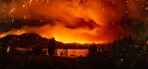 un incendie intense se propageant sur une colline et dans le paysage environnant, avec des flammes orange vif, une épaisse fumée rouge orangé et des braises lumineuses remplissant le ciel