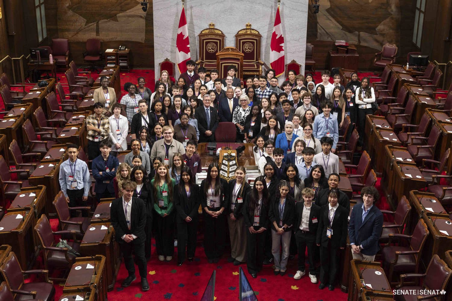 Un grand groupe de personnes se fait prendre en photo autour d’une table dans la Chambre du Sénat.