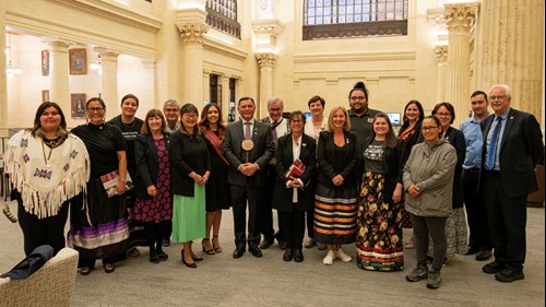Des sénateurs, l’aîné Simon Brascoupé et les participants de Voix de jeunes leaders autochtones posent pour une photo de groupe dans le salon des sénateurs de l’édifice du Sénat du Canada.