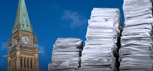 Large stacks of paper beside the Peace Tower on Parliament Hill under a blue sky.