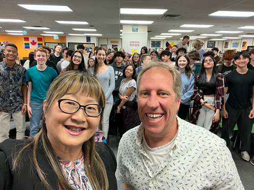 Senator Yonah Martin and teacher Stephane Ethier taking a selfie in a classroom with students standing behind them.