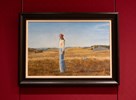 Une peinture d’une femme debout dans un champ d’herbes sèches, avec des collines et un ciel bleu en arrière-plan.